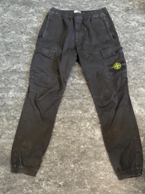 Svarta cargobyxor från Stone Island - Säljer ett par svarta cargobyxor från Stone Island med klassisk patch på benet. Byxorna har flera fickor, resår i midjan och vid bensluten samt en avslappnad passform. Perfekta för en streetwear-look och till dig som gillar funktionella detaljer. Nypris 3199 kr, har även kvitto  köpt hos Johnells. ÄKTA 