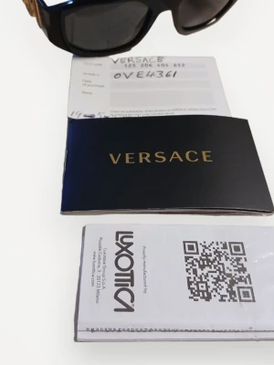Versace svarta solglasögon med guld - Snygga svarta solglasögon från Versace med ikoniska guldfärgade Medusa-detaljer på skalmarna. Glasögonen har en klassisk rektangulär form och levereras med originaletui. Perfekt accessoar för dig som vill sticka ut. Har kvittot också 