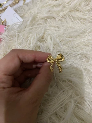 Guldfärgad ring med rosett, rostfritt stål - Snygg guldfärgad ring i metall med en stor, detaljerad rosett framtill. Ringen har en öppen baksida vilket gör den justerbar i storlek. Perfekt accessoar för dig som gillar söta och trendiga detaljer.