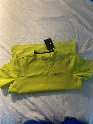 Gul tränings-tshirt från Nike - Snygg gul tränings-tshirt från Nike med rund halsringning och reflekterande detaljer på axlarna. Tillverkad i ett lätt och ventilerande material som passar perfekt för löpning eller gym. Klassisk Nike-logga på bröstet.