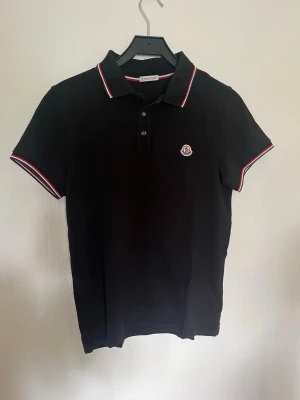 Moncler piké - Säljer nu denna väldigt fina moncler piké. Storlek på denna är S. Skick 9/10 inga skador. Färgen är en marinblå färg. För fler frågor eller funderingar är de bara att höra av sig. 