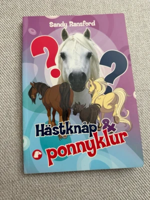 Hästknåp & ponnyklur av Sandy Ransford - Rolig och färgglad bok med quiz och kluriga frågor om hästar och ponnyer. Omslaget är lila och blått med illustrationer av hästar och stora frågetecken. Perfekt för dig som gillar hästar och vill testa dina kunskaper eller utmana kompisar.