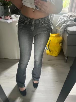 Grå bootcut jeans från Levi's - Säljer ett par snygga grå bootcut jeans från Levi's med slitna detaljer och klassiska fem fickor. Jeansen har låg midja och är tillverkade i stretchigt denim för en bekväm passform. Perfekta för dig som gillar en avslappnad men trendig stil.