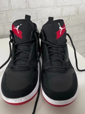 Svarta Air Jordan sneakers - Snygga svarta Air Jordan sneakers med högt skaft, vita sulor och röda detaljer. Skorna har klassisk Jordan logga på plösen och siffran 23 på sidan. Tillverkade i en mix av läder och syntetmaterial för en clean och sportig look.