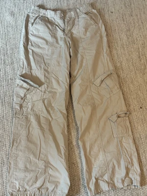 Beiga low waist cargobyxor - Säljer ett par beiga cargobyxor med avslappnad passform och resår i midja och benslut. Byxorna har flera stora fickor på sidorna och är low waisted.