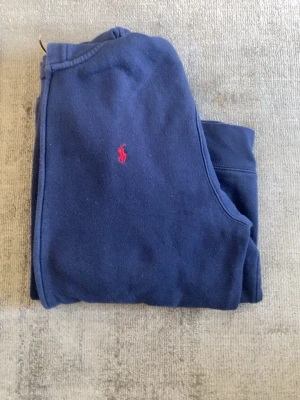 Mörkblå hoodie från Polo Ralph Lauren - Klassisk mörkblå hoodie från Polo Ralph Lauren med dragkedja, huva och två fickor framtill. Ikoniska röda logotypen broderad på bröstet. Tillverkad i mjuk bomullsblandning som är skön att ha på sig. Perfekt för en avslappnad och stilren look.
