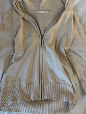 Beige hoodie med dragkedja - Säljer en stilren beige hoodie från COS med dragkedja framtill och huva. Hoodien har ribbade muddar vid ärmslut och nederkant samt en avslappnad passform. Perfekt för en chill och enkel look.