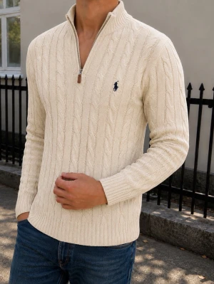 Beige kabelstickad tröja Polo Ralph Lauren - Kabelstickad beige tröja från Polo Ralph Lauren med halv dragkedja och hög krage. Tröjan har det klassiska mörkblå logobroderiet på bröstet och ribbade muddar. Tillverkad i mjukt material som ger en stilren och tidlös look.