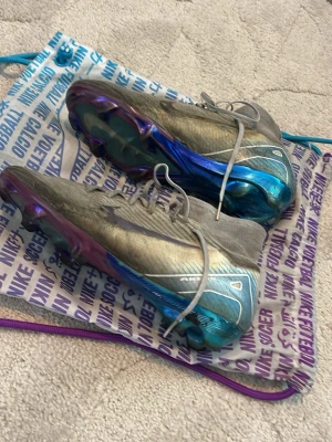 Nike Mercurial Elite  - Säljer ett par Nike Mercurial fotbollsskor i vitt med metallicblå och lila detaljer. Skorna har snörning, låg profil och en sula med dobbar för bra grepp på planen. Swoosh-logga på sidan och cool design som sticker ut på fotbollsplanen. Det är elite och en ovanlig modell från chrome släppet och nypris va ca 3700 om jag minns rätt, kvitto finns. Hör av er vid fundering. Skorna är i bra skick och är endast smutsiga och lite av färgen under skon har släppt annars bra.