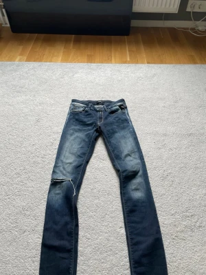 Mörkblå slim jeans med slitning - Säljer ett par mörkblå slim jeans med slitning på vänster knä och snygga tvättade detaljer. Jeansen har klassisk femficksdesign och slim  passform. Perfekta för dig som gillar en avslappnad men trendig stil.