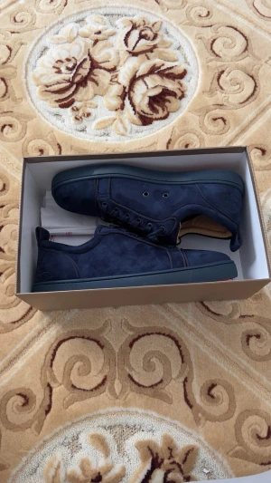 Mörkblå sneakers från Louboutin - Snygga mörkblå sneakers från Christian Louboutin med klassisk låg profil och ikonisk röd sula. Skorna är tillverkade i mocka och har matchande mörkblå snörning. Perfekta för dig som vill sticka ut med exklusiv design och premiumkänsla.
