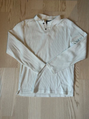 Vit henley från H&M i bomull - Vit långärmad henley från H&M i slim fit-modell. Skjortan har knappar vid halsen och är tillverkad i ett mjukt bomullstyg med diskret struktur. Perfekt för en clean och stilren look.