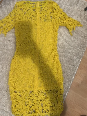Gul spetsklänning med kort ärm - Säljer en superfin gul klänning i spets med korta ärmar och rund hals. Klänningen har ett vackert blommigt spetsmönster och är figurnära med kort längd. Perfekt för sommarens alla tillfällen! Står storlek L men skulle säga S/M