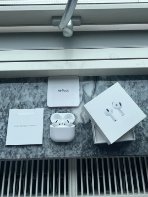 Apple AirPods med laddningsetui - Säljer ett par vita Apple AirPods med trådlöst laddningsetui. Snygg och stilren design i blank plast, perfekt för dig som vill ha smidiga hörlurar till mobilen. Kommer i originalförpackning med tillhörande manualer.