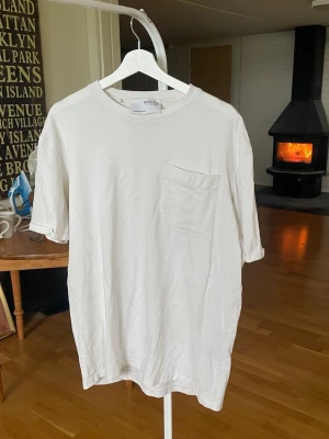 Vit t-shirt från Selected Homme - Klassisk vit t-shirt från Selected Homme med rund halsringning och en bröstficka. Tillverkad i mjuk bomull och har en avslappnad passform med korta ärmar. Perfekt basplagg till garderoben. Stl L