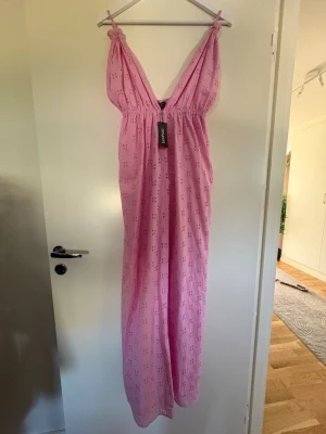 Ljusrosa långklänning Boohoo - Söt ljusrosa långklänning från Boohoo med broderade blommor och smala axelband som knyts upptill. Klänningen har v-ringning och resår i midjan för en bekväm passform. Perfekt för sommarens alla tillfällen!