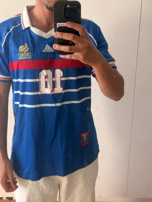 Frankrike 98’ Zidane tröja - Säljer en ikonisk blå fotbollströja från Adidas, Frankrikes landslag, med nummer 10 och Zidane på ryggen. Säljer pga storlek (kolla profil beskrivningen). Perfekt inför VM!!