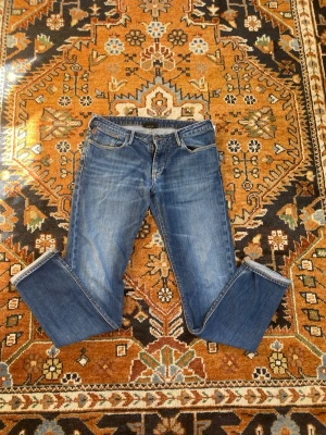 Emporio Armani - Säljer ett par klassiska blå jeans från Emporio Armani. Storlek 33/34. Skriv om mått och prisrekommendationer! Svarar så fort som möjligt på frågor! Väldigt bra skick, däremot välfigt litet slitet hål previs vid slutat av vänstra benet.