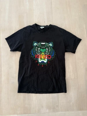 Svart Kenzo t-shirt med tigertryck - Snygg svart t-shirt från Kenzo med det ikoniska tigerhuvudet i färgglatt tryck på bröstet och texten 'KENZO PARIS'. Klassisk passform och rund hals.