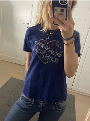 Mörkblå Zadig&Voltaire - Mörkblå t-shirt med korta ärmar och ett stort hjärtmotiv i glittriga stenar på bröstet. T-shirten har en klassisk passform och rund halsringning. Perfekt för dig som vill ha något unikt och snyggt i garderoben.💕