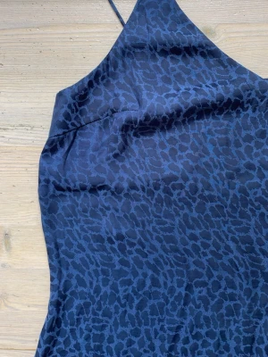Mörkblå leopardmönstrad satintopp - Mycket bra skick. Osäker på material, om det inte är satin så är det någon som är åt det hållet. Kommer är tunt, fladdrar och glansigt. I linnet står storlek 42 men vid axelbanden (se bästisars bild) så är dit sytt så att banden blev lite kortare och nu är linnet mer som en inte tajt S.