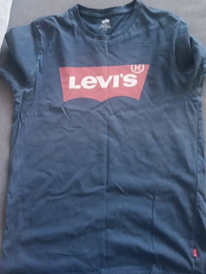 Blå Levi's t-shirt med logga - Säljer en klassisk blå t-shirt från Levi's med den ikoniska röda loggan framtill. T-shirten har rund halsringning och korta ärmar. Tillverkad i mjuk bomull som är skön att bära hela dagen.