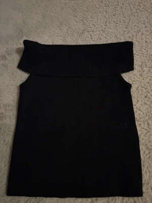 Svart ribbad offshoulder tubtopp - Säljer en svart ribbad tubtopp med bred offshoulder-krage. Toppen är ärmlös och har en tight passform som framhäver axlarna. Perfekt för dig som gillar minimalistisk och stilren look. Materialet känns mjukt och stretchigt.