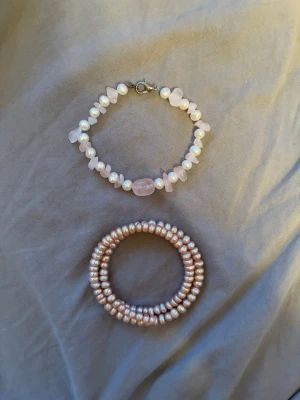 Två armband med pärlor och stenar - Säljer två snygga armband, ett med vita pärlor och ljusrosa stenar samt ett spiralformat armband med små rosa pärlor.