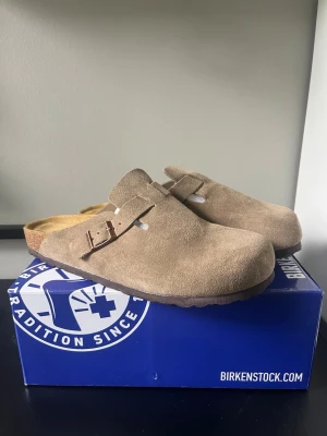 Birkenstock  - Säljer ett par helt oanvända Birkenstock Boston tofflor i beige mocka. De har en rundad tå och är riktigt sköna att glida i. Perfekta för dig som gillar stilrena och bekväma skor. Skriv till mig om snabba affärer eller om mer info! Box tillkommer