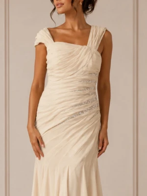 Champagnefärgad långklänning med drapering - Elegant långklänning i champagnefärg med draperad överdel och subtila glittriga detaljer. Klänningen har figurnära passform upptill och faller mjukt från höften. Perfekt för bal eller festligare tillfällen.