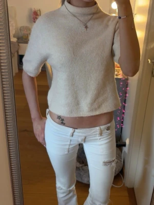 Beige-rosa  kortärmad polotröja - Säljer en vit, mjuk och stickad polotröja med korta ärmar och rak passform. Tröjan har en hög krage och är perfekt för lager-på-lager-stil. 