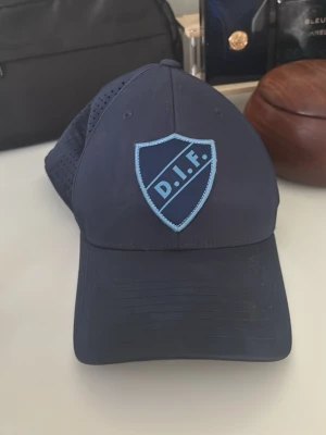Mörkblå DIF keps från CCM - Snygg mörkblå keps med DIF-logga i ljusblått framtill och gul CCM-brodyr på sidan. 