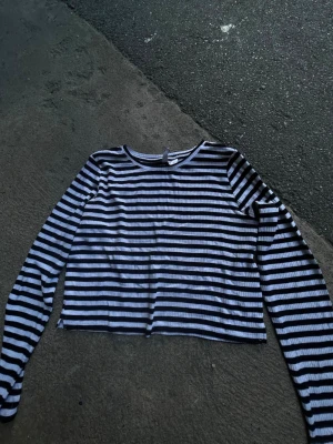 Randig långärmad topp från H&M Divided - Säljer en svartvit randig långärmad topp från H&M Divided. Toppen är ribbad och croppad med klassisk rund halsringning. Perfekt att styla med jeans eller kjol för en chill look.