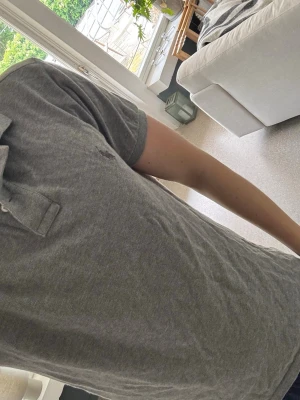 Grå pikétröja Polo Ralph Lauren M - Säljer en grå pikétröja från Polo Ralph Lauren i slim fit-modell, vilket gör att den blir tajt vid armarna. Tröjan har klassisk krage och korta ärmar, perfekt för en clean och enkel stil. Tillverkad i mjuk bomull som känns skön mot huden.