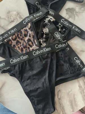 Svarta trosor med leopardmönster Calvin Klein - Säljer flera snygga svarta trosor från Calvin Klein med bred resår och logotyp. Några har leopardmönster och meshdetaljer, andra är helsvarta med subtila blommönster. Materialet är mjukt och stretchigt, perfekt för dig som vill ha både stil och komfort.