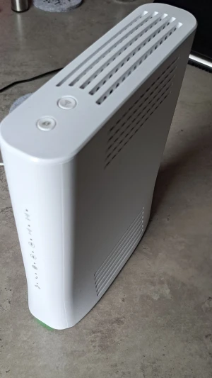 Vit coaxrouter/modem - Säljer en vit router eller modem med avlånga ventilationshål på sidorna och ovansidan. Den har en modern, rundad design och knappar på toppen. Materialet är plast och den har LED-indikatorer på framsidan.