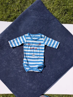 Långärmad Body strl 50 bebis från name it baby Organic cotton - Knappar vid hals  Blå och vit randig Inga hål eller fläckar, eventuellt lite blekare än ny Se material på bild   Kanin liknande på magen