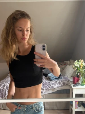 Svart ribbad croppad linnetopp - Snygg svart croppad linnetopp med ribbad struktur. Toppen är ärmlös och har en tight passform som framhäver midjan. Perfekt att matcha med jeans eller kjol för en trendig look.