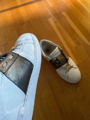 Valentin opens - Snygga vita valentino sneakers med bred svart läderdetalj över mitten och vita snören. Skorna har en klassisk låg profil, perfekt för en stilren look perfekta nu till sommaren. Materialet är läder och designen är enkel men modern. ‼️OBS box och dustbag ingår inte ‼️bild på  kvitto går att få. Bara att höra av dig vid funderingar