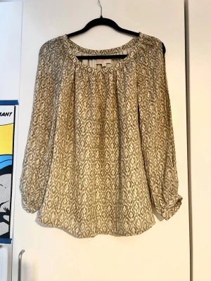 Mönstrad blus 100% silke från Michael Kors XS - Snygg beige och vit blus i 100% silke från Michael Kors i storlek XS. Blusen har ett grafiskt mönster, rund halsringning och långa öppna ärmar med lätt puff vid ärmslut. Tillverkad i ett tunt, luftigt material i silke som ger en avslappnad men stilren look.