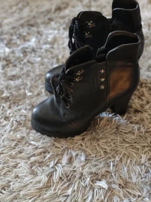 Svarta boots med stjärndetaljer - Säljer ett par svarta boots med snörning och chunky klack. Bootsens sidor är dekorerade med coola silverfärgade stjärnor. Tillverkade i skinnimitation och perfekta för dig som vill ha en edgy look.