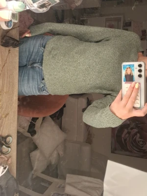 Grön stickad tröja med rund hals - Mysig grön stickad tröja med rund hals och långa ärmar. Tröjan har en enkel, klassisk design och är tillverkad i ett mjukt, melerat garn som ger en avslappnad look. Perfekt att matcha med jeans för en chill vardagsstil.