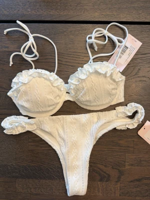 Vit bikini med volang från Nelly - Supersöt vit bikini från Nelly med volangdetaljer på både överdel och underdel. Underdelen är xs och överdelen 75A