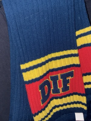 Djurgården halsduk i blå, gul och röd - Säljer en ribbstickad halsduk från Djurgårdens IF i blått, gult och rött. Halsduken har DIF-logga och broderat klubbmärke med texten 'Djurgårdens Hockeyförening 1891'. Perfekt för att visa ditt stöd på matchen!