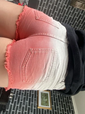 Ombre shorts med fransig kant - Säljer ett par snygga ombre shorts i vitt och rosa med hög midja. Shortsen har fransig kant nertill, klassiska fickor både fram och bak samt knapp och dragkedja framtill. Perfekta för sommaren och ger en riktigt fräsch look!