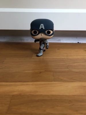 Captain America Funko Pop figur - Cool Captain America Funko Pop figur med mörkblå mask och vit 'A' på pannan. Figuren har en grå och svart dräkt med röda detaljer, och är tillverkad i vinyl. Perfekt som accessoar till cosplay eller maskerad. Skicka ett prisförslag om ni är intresserade! 