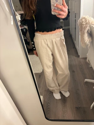 Beige linnebyxor från SHEIN - Säljer ett par beige linnebyxor från SHEIN med breda ben och elastisk midja. Materialet är lätt och luftigt, perfekt för en avslappnad stil. Byxorna har en enkel design utan fickor och är tillverkade i linneblandning.