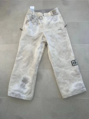 Volcom vita snowboardbyxor - Säljer ett par vita snowboardbyxor från Volcom med grått mönster och bred passform. Byxorna har två knappar i midjan, fickor fram och bak samt en DUO patch på benet. Perfekta för vintersport och har slitstarka material.