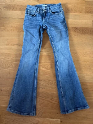 Blå bootcut jeans med broderade fickor - Säljer ett par blå bootcut jeans med snygga broderade detaljer på bakfickorna. Jeansen har klassisk femficksdesign och är tillverkade i denim med lätt stretch. Perfekt för dig som gillar retrostil och vill ha ett par jeans med cool passform.