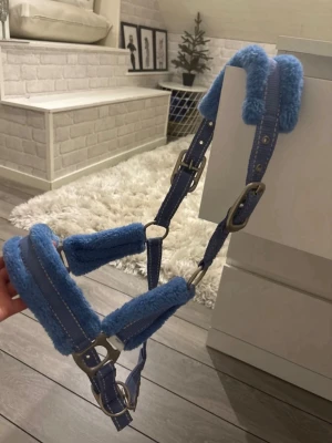 Blå fluffig grimma till häst aldrig andvänt  - Säljer en blå grimma med mjukt fluffigt foder på insidan, perfekt för att ge extra komfort till hästen. Grimman har metallspännen och justerbara remmar. Materialet är en kombination av slitstark textil och syntetpäls. Passar till häst och är både snygg och praktisk.